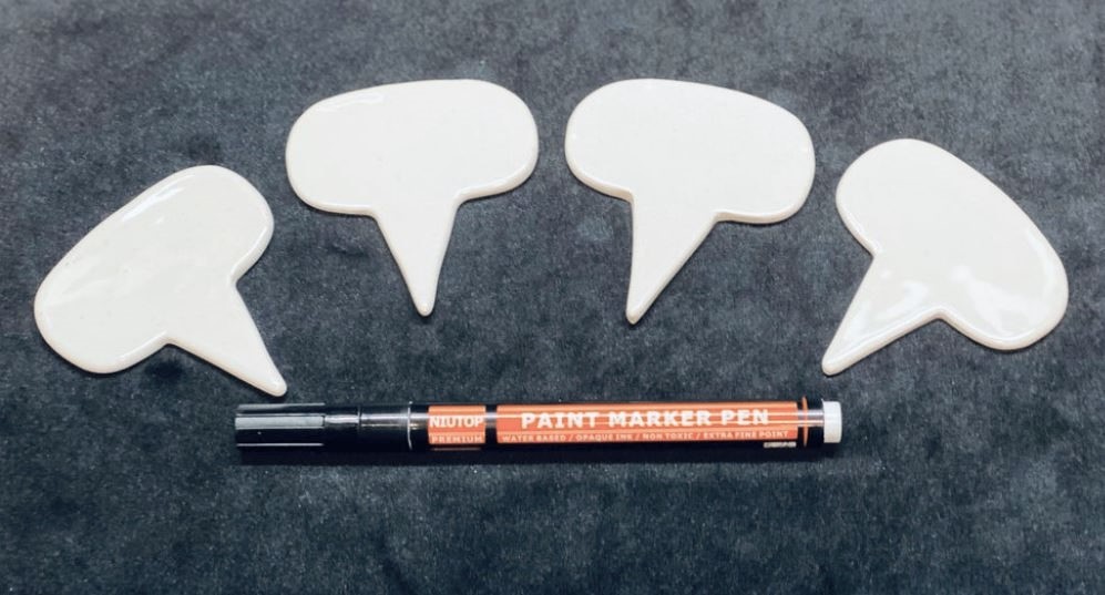 A picture of four white porcelain cheese markers with a paint marker under them
