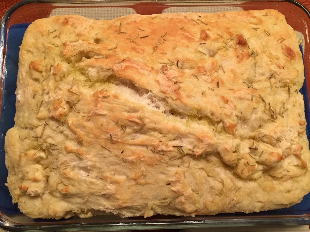 A picture of a loaf of focaccia bread with rosemary sprinkled on top in a glass dish