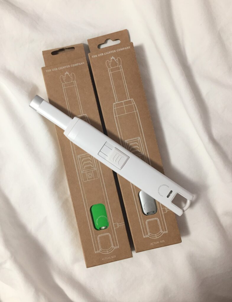 A picture of a white USB candle lighter on top of two cardboard boxes with lighters inside
