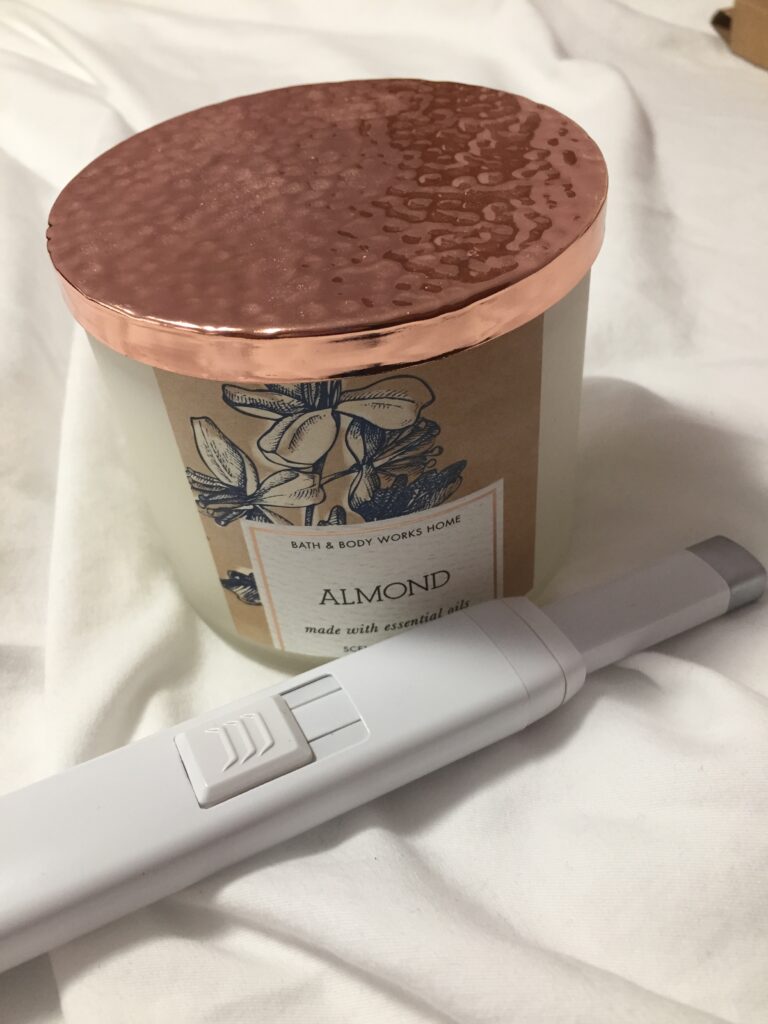 A picture of a reusable USB lighter next to a Bath and Body Works Almond candle