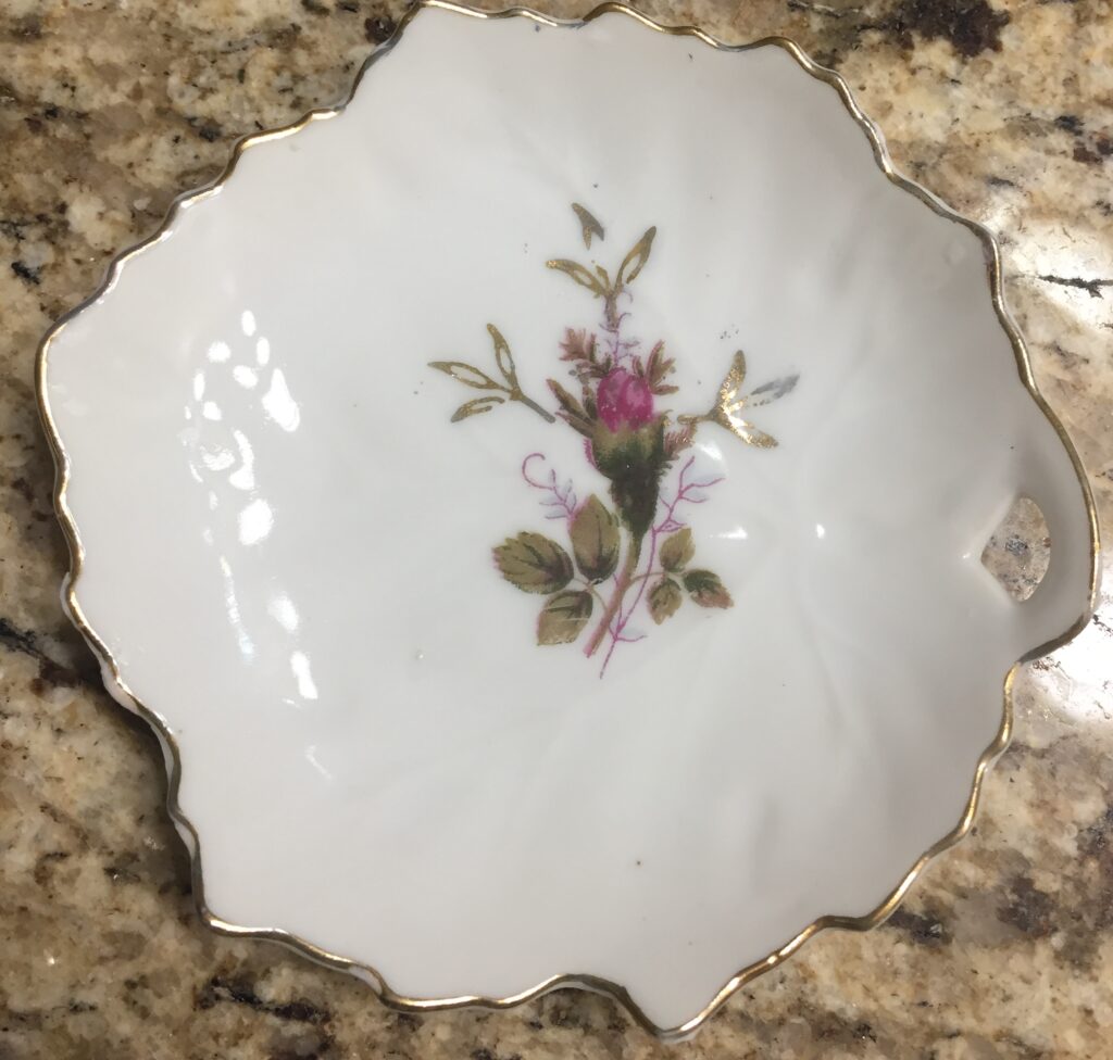 A picture of a white glass soap dish with floral details and gold around the edges