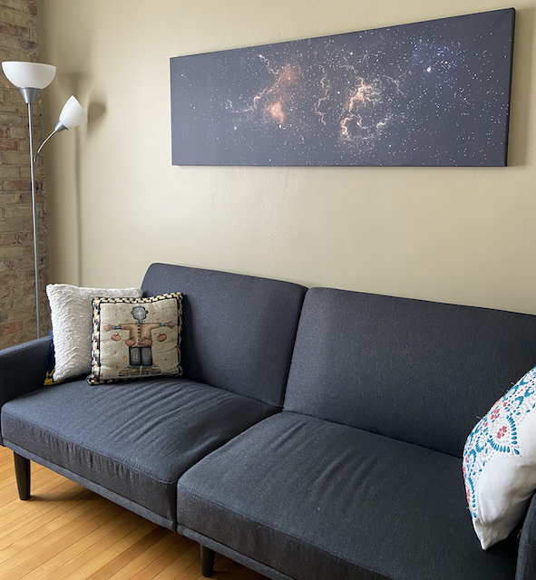 A picture of a Photowall canvas outer space print hanging on the wall above a gray futon