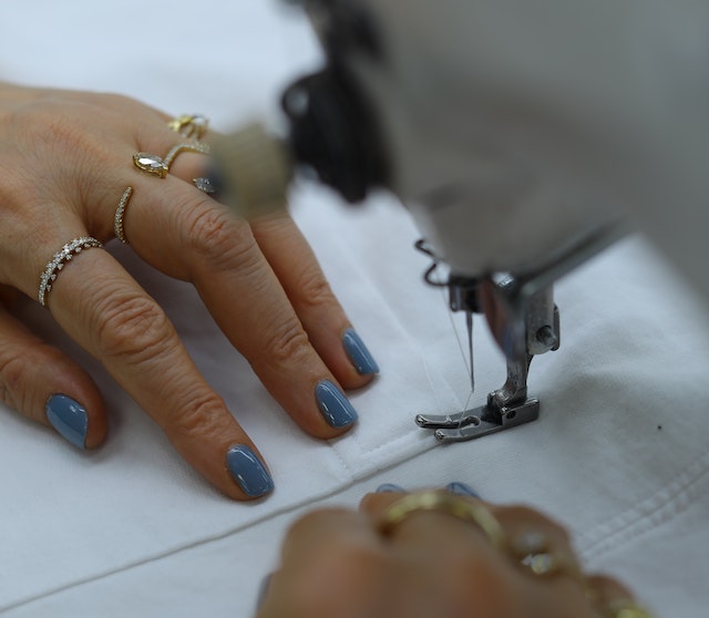 A picture of two hands guiding the needle of a sewing machine through white fabric