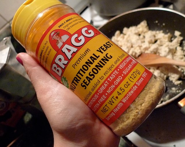 A picture of a hand holding a container of nutritional yeast