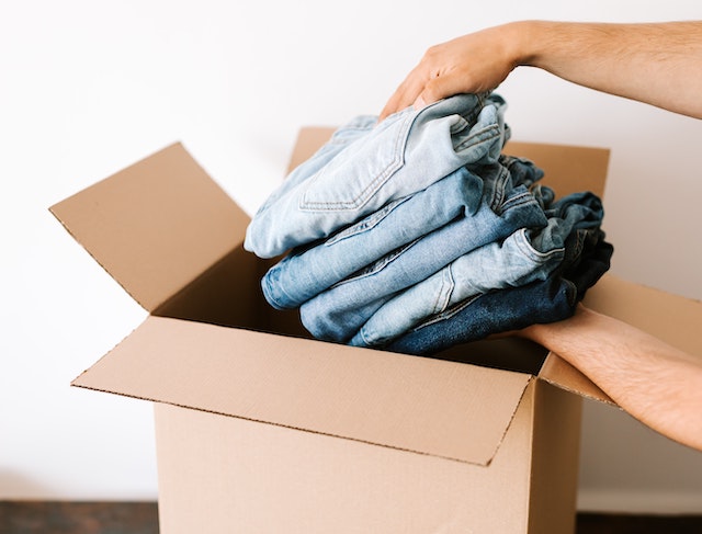 A picture of a box of donations with hands putting in a pile of jeans