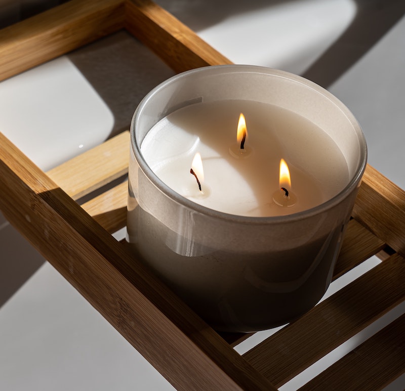 A picture of a lit three wick candle, sitting on top of a wooden tray