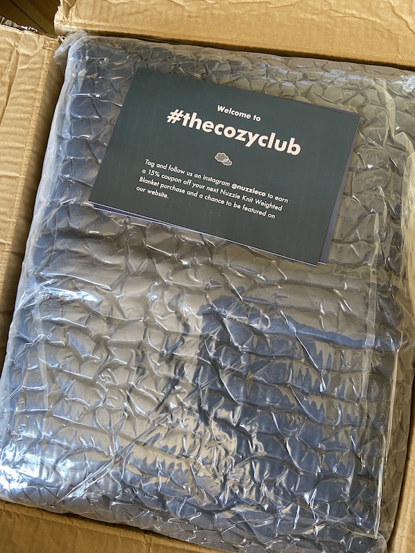 A picture of a Nuzzie knit weighted blanket when it arrived, vacuumed sealed in a box
