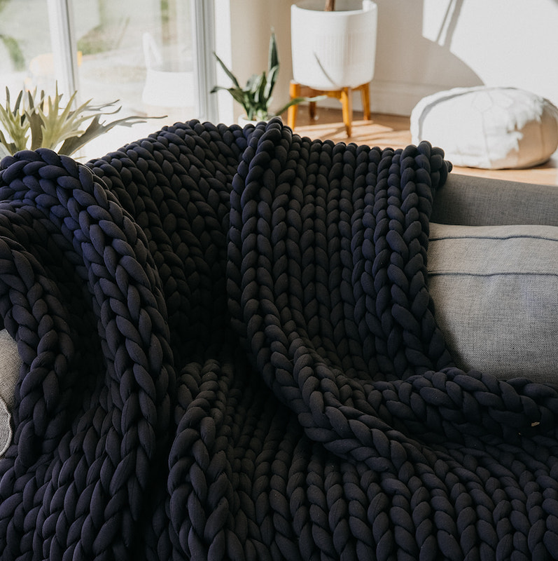 A picture of a Nuzzie knit weighted blanket on a couch